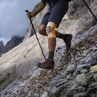 Vandrare med stavar och Sports Outdoor Knee Support på stenig stig